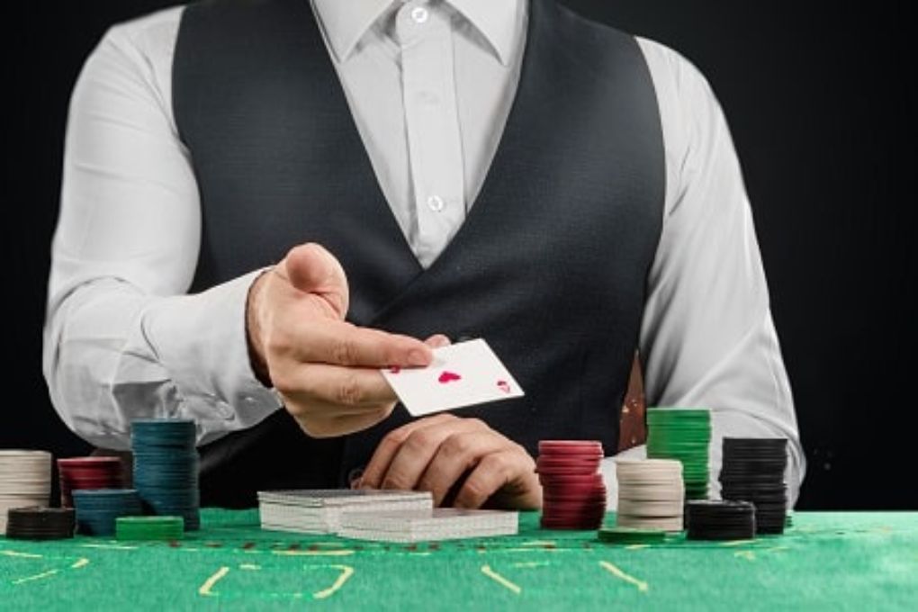 Casino dealer holding card in front of green table and casino chips